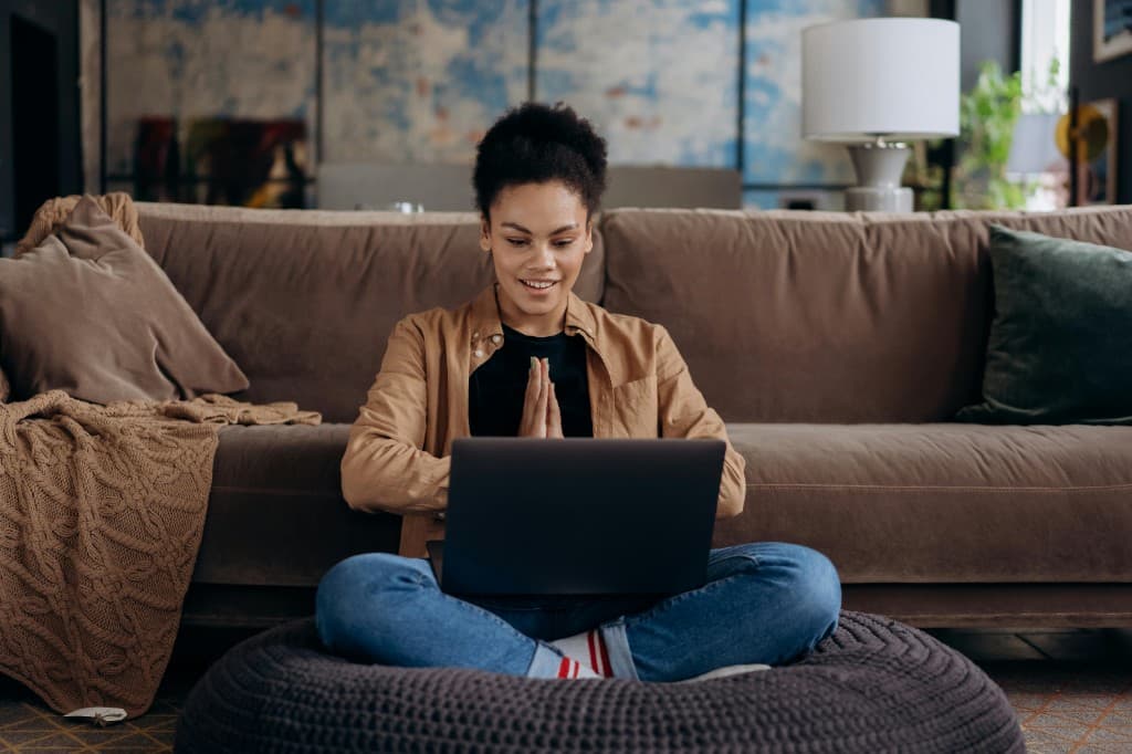 Person in prayer gesture with laptop in a cozy space